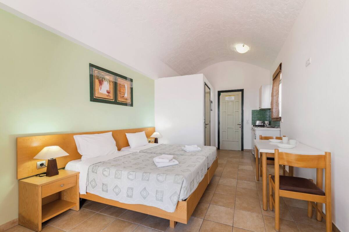 A hotel room with a bed, bedside table, lamp, and a small desk with a chair.