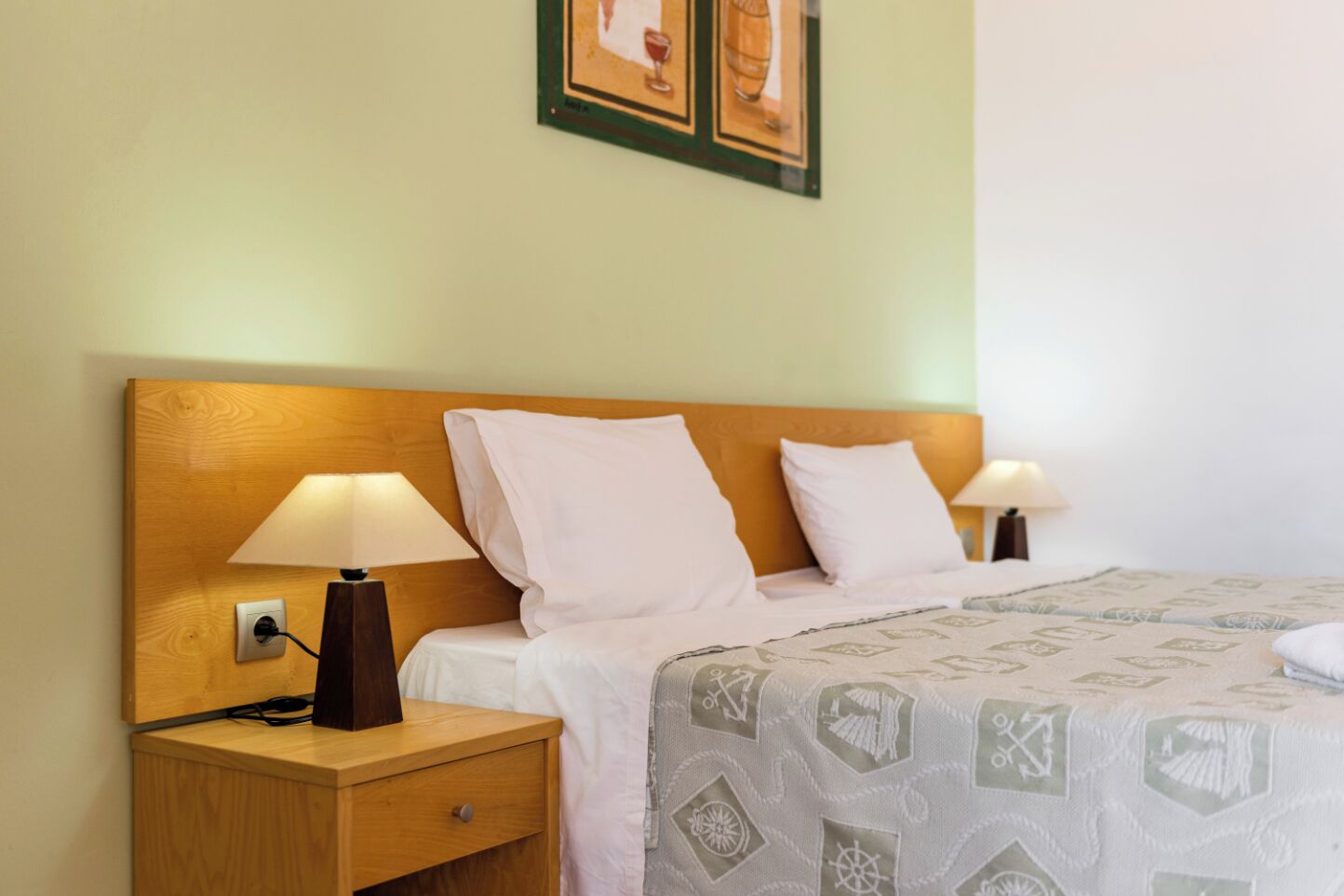 A neatly made bed with a patterned bedspread, two bedside lamps, a wooden nightstand with a drawer, and a framed picture above the bed.