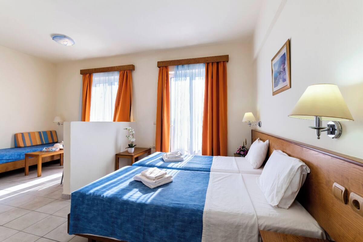 A hotel room with two beds, a sofa, a small table, and a lamp.