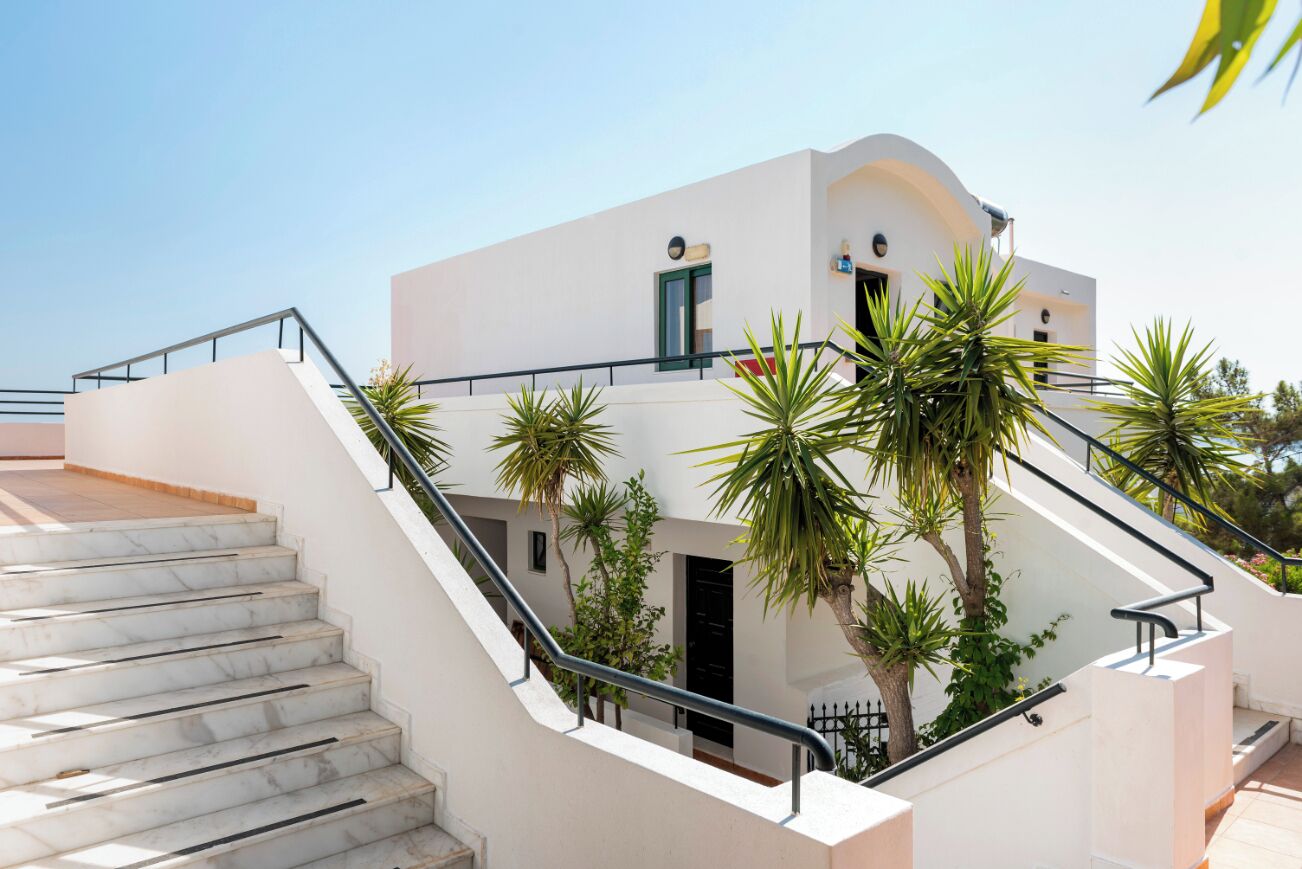 Ein modernes Gebäude mit weißer Fassade, einer Treppe, die zu einem Balkon führt, und mehreren Palmen.