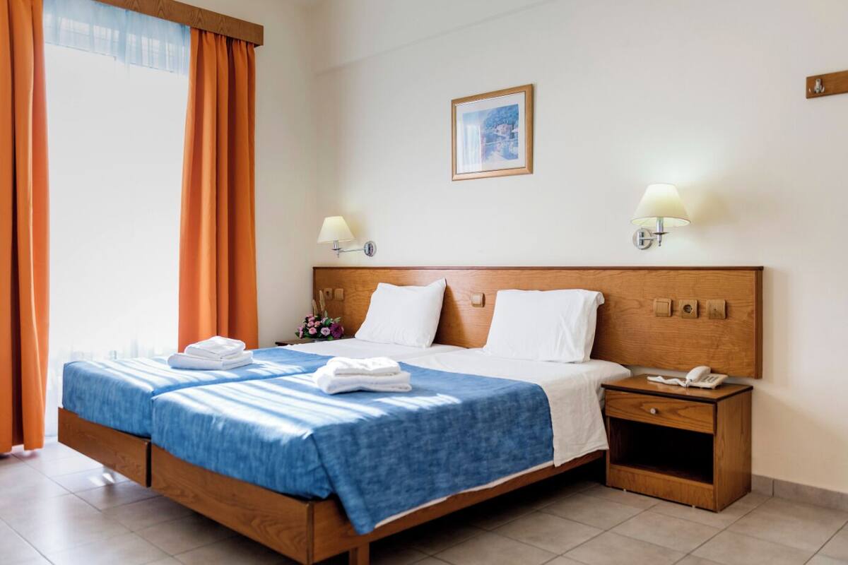 A hotel room with a wooden bed, two bedside lamps, a small bedside table with a phone, and a framed picture on the wall.