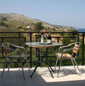 A round table with two chairs, a bottle of wine, and a glass on a balcony overlooking a coastal landscape. - Starlight Hotel (Kefalonia)