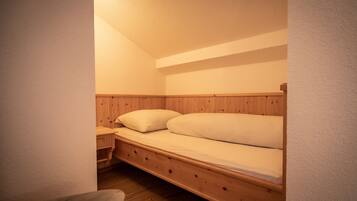 Una habitación pequeña y acogedora con una cama nido de madera, una mesita de noche y una silla.