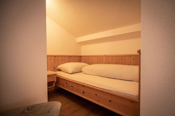 A small, cozy room with a wooden bunk bed, a nightstand, and a chair.