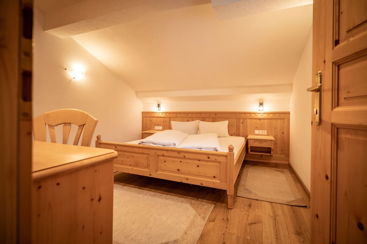 A bedroom with a wooden bed, bedside tables, a chair, and a door.