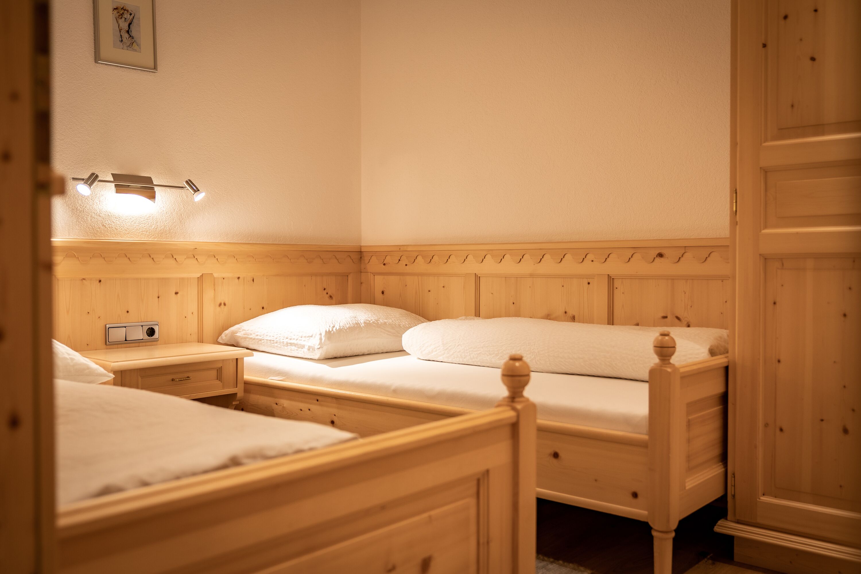 Un dormitorio con dos camas de madera, una mesita de noche con una radio y una lámpara fijada a la pared.
