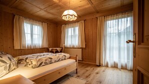 Una habitación de madera con cama, mesita de noche, radiador y ventana con cortinas.