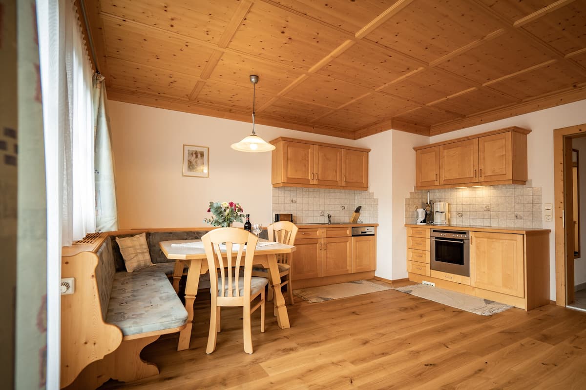 A cozy kitchen with wooden cabinets, a dining area with a bench, and a tiled backsplash.