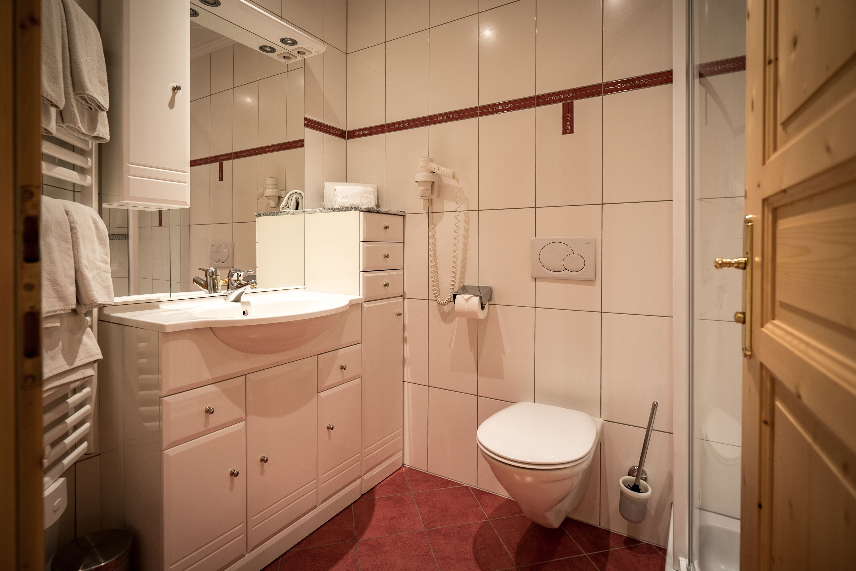 A bathroom with a white sink, mirror, and toilet. There is a towel rack and a shower head on the wall.