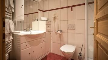 A bathroom with a white sink, mirror, and toilet. There is a towel rack and a shower head on the wall.