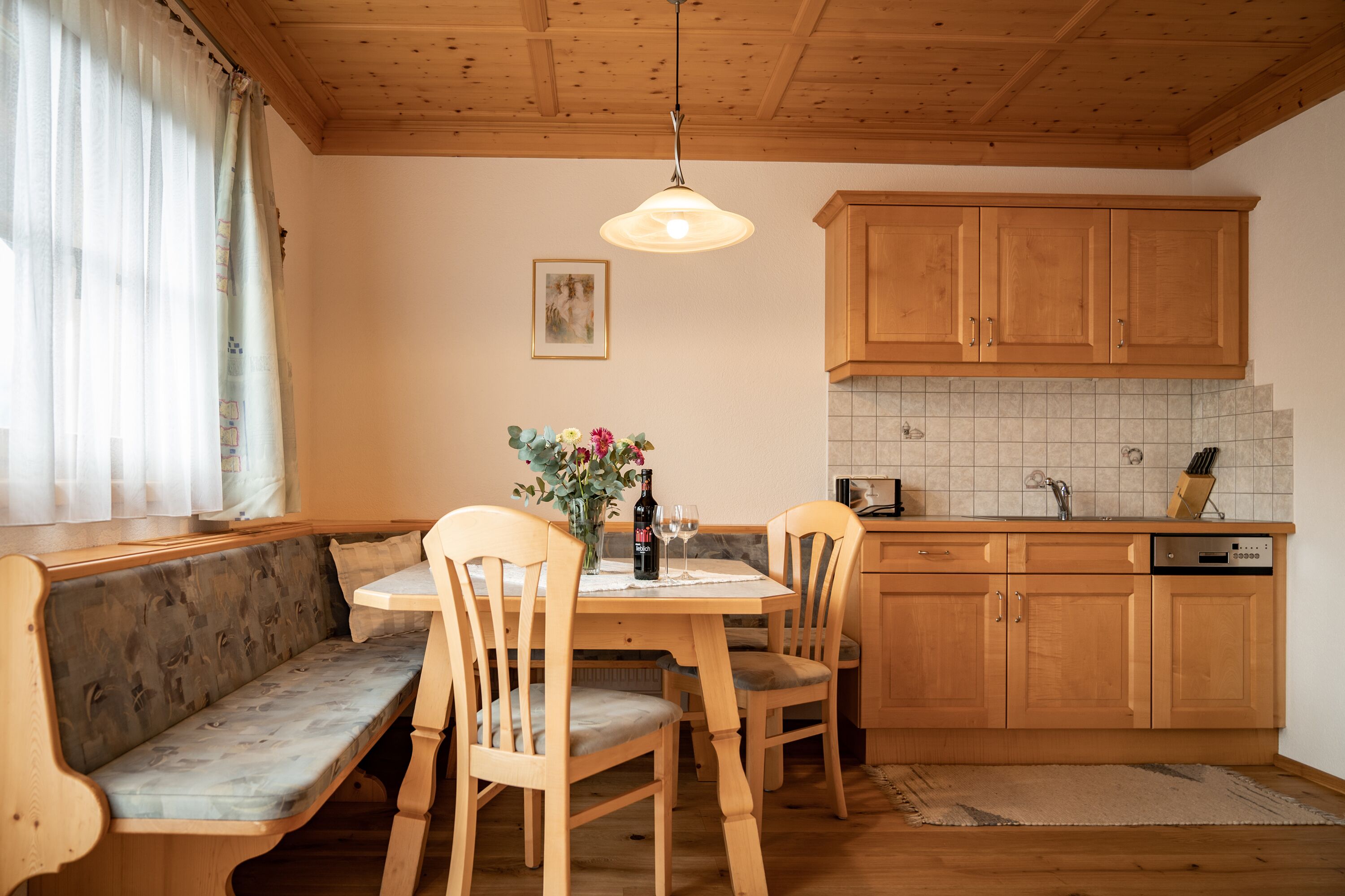Une cuisine chaleureuse avec des meubles de rangement en bois, une table à manger avec des chaises et un banc.