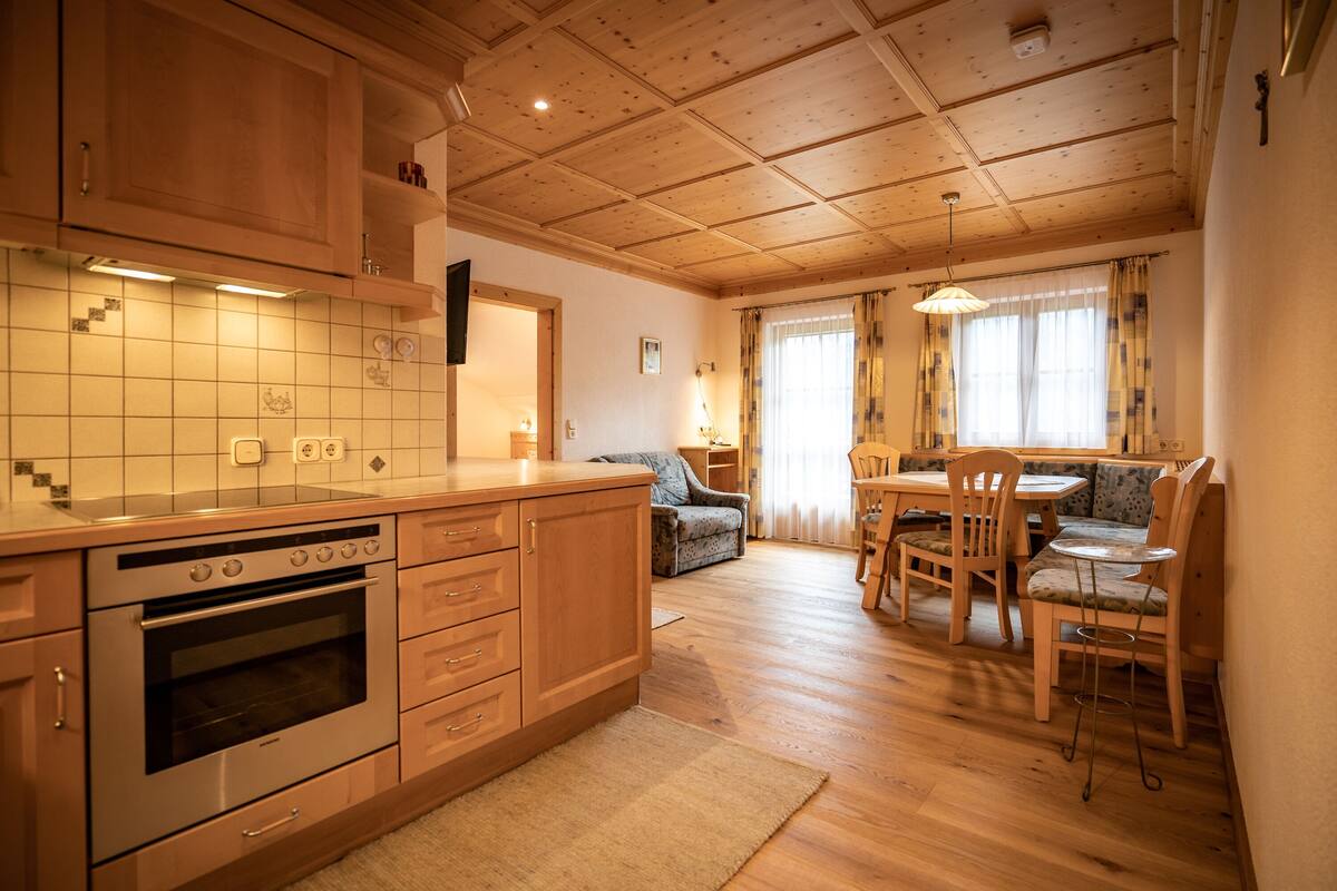 A kitchen with wooden cabinets, a built-in oven, and a dining area with a table and chairs.