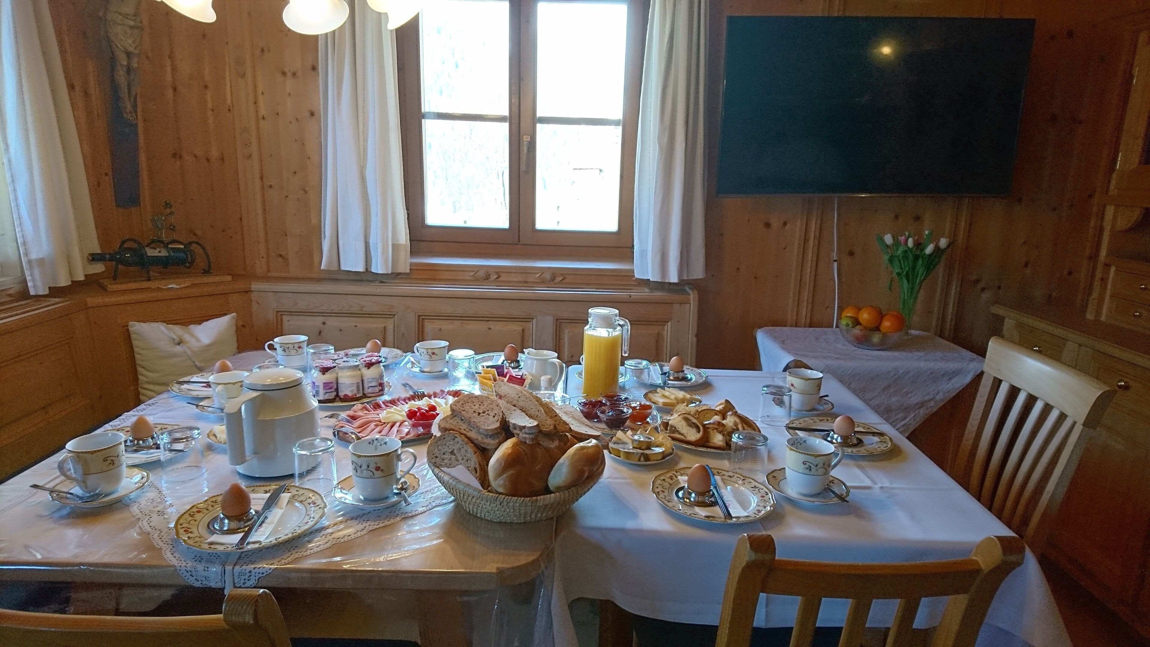 A wooden dining room with a table set for breakfast, including bread, eggs, and fruit.
