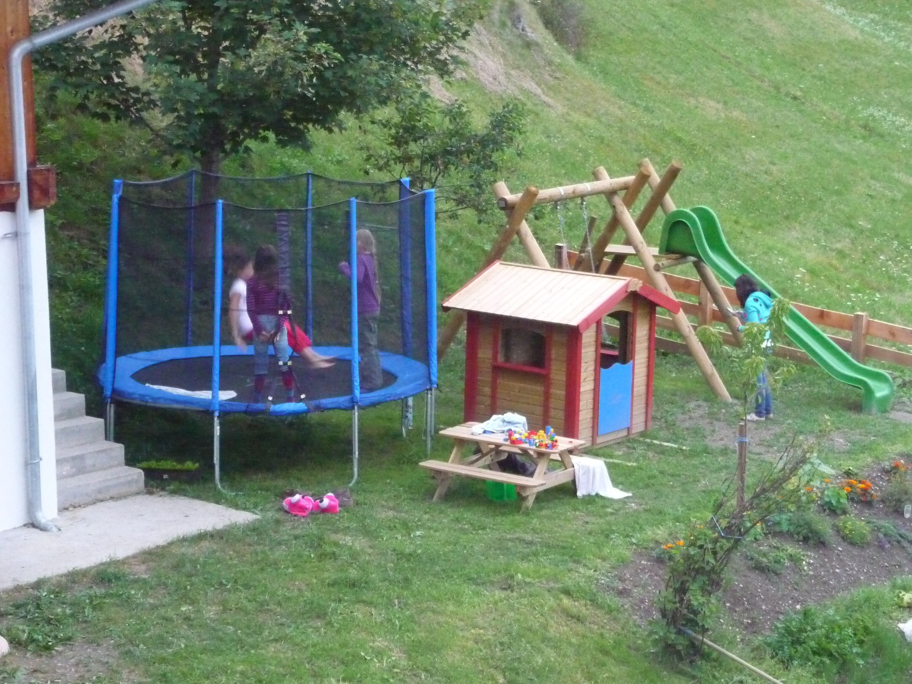 A playground with a trampoline, a wooden playhouse, and a slide.