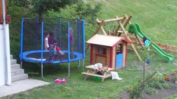 A playground with a trampoline, a wooden playhouse, and a slide.
