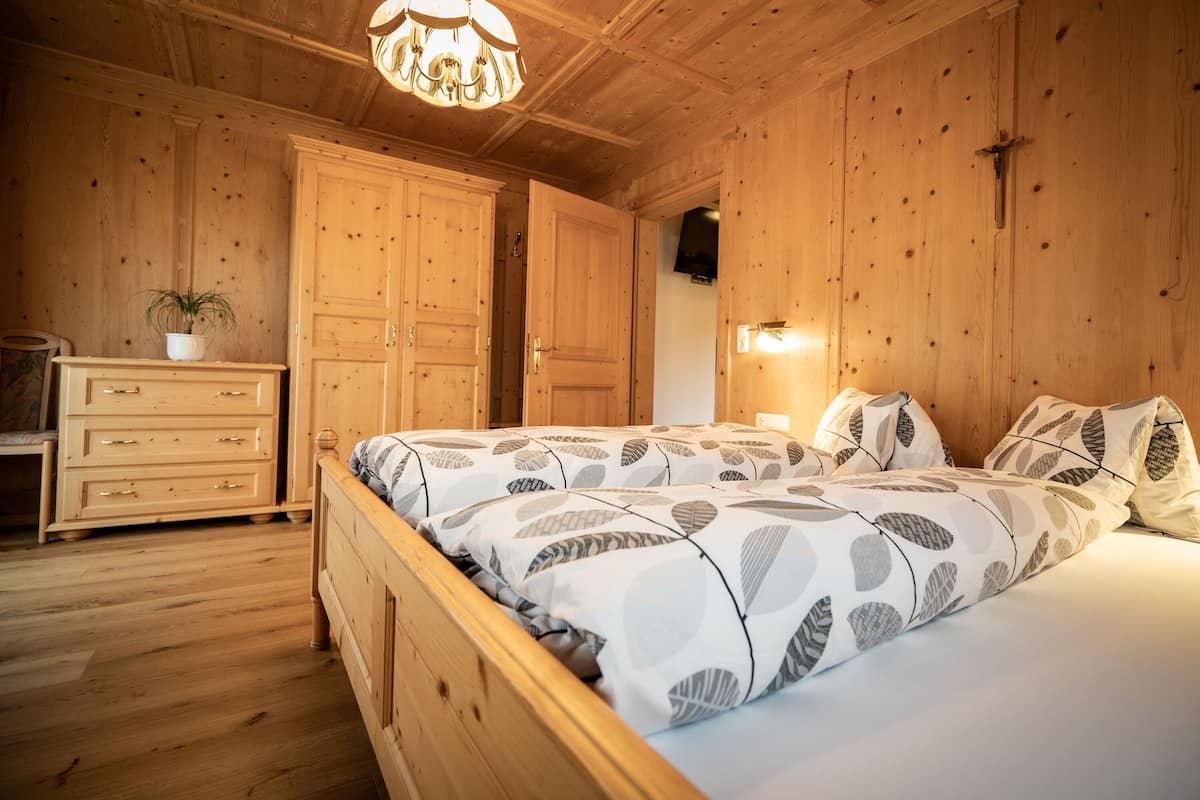 A wooden-paneled bedroom with a bed, dresser, and a potted plant.
