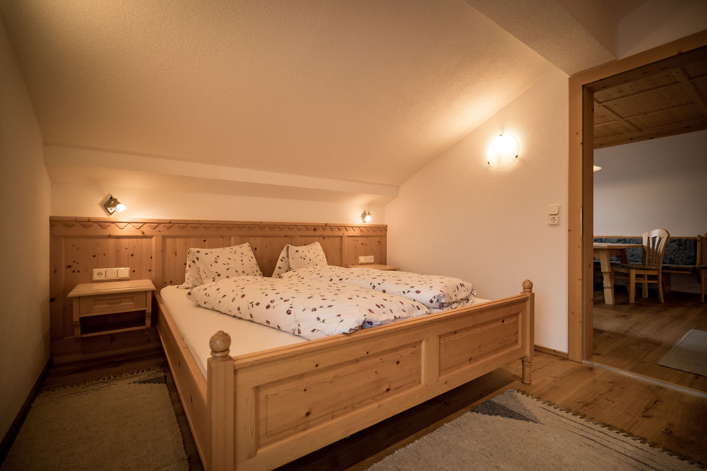 Un dormitorio con cama de madera, mesitas de noche y un espejo que refleja un comedor.