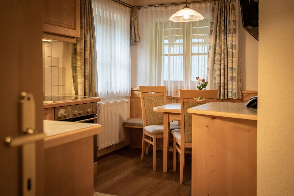A compact kitchen with wooden cabinets, a stove, and a dining area with two chairs.