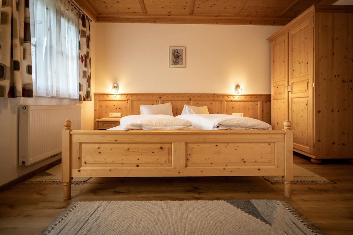 A wooden bed with two bedside tables, a radiator, and a wardrobe in a room with wooden walls and ceiling.
