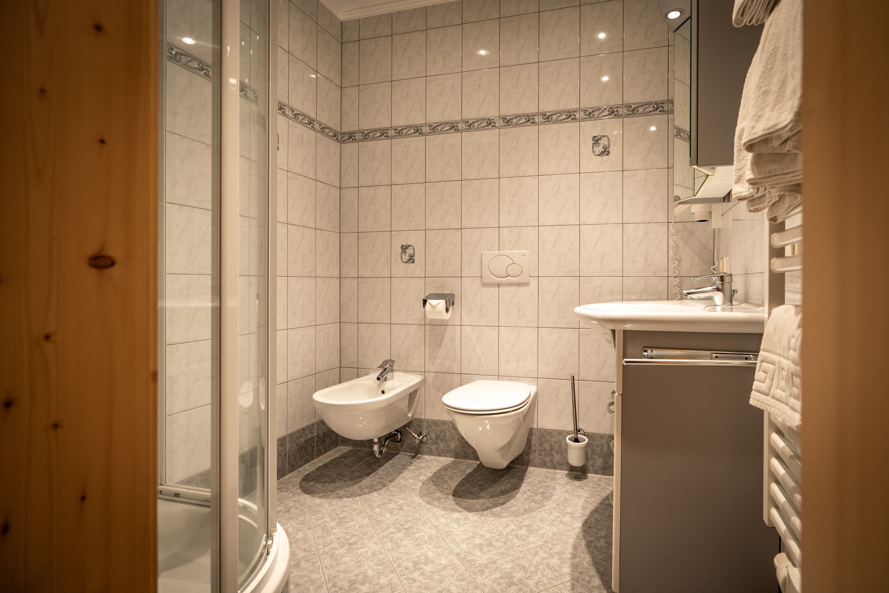 Un baño con cabina de ducha de vidrio, un bidé, un inodoro y un lavamanos con toallero.
