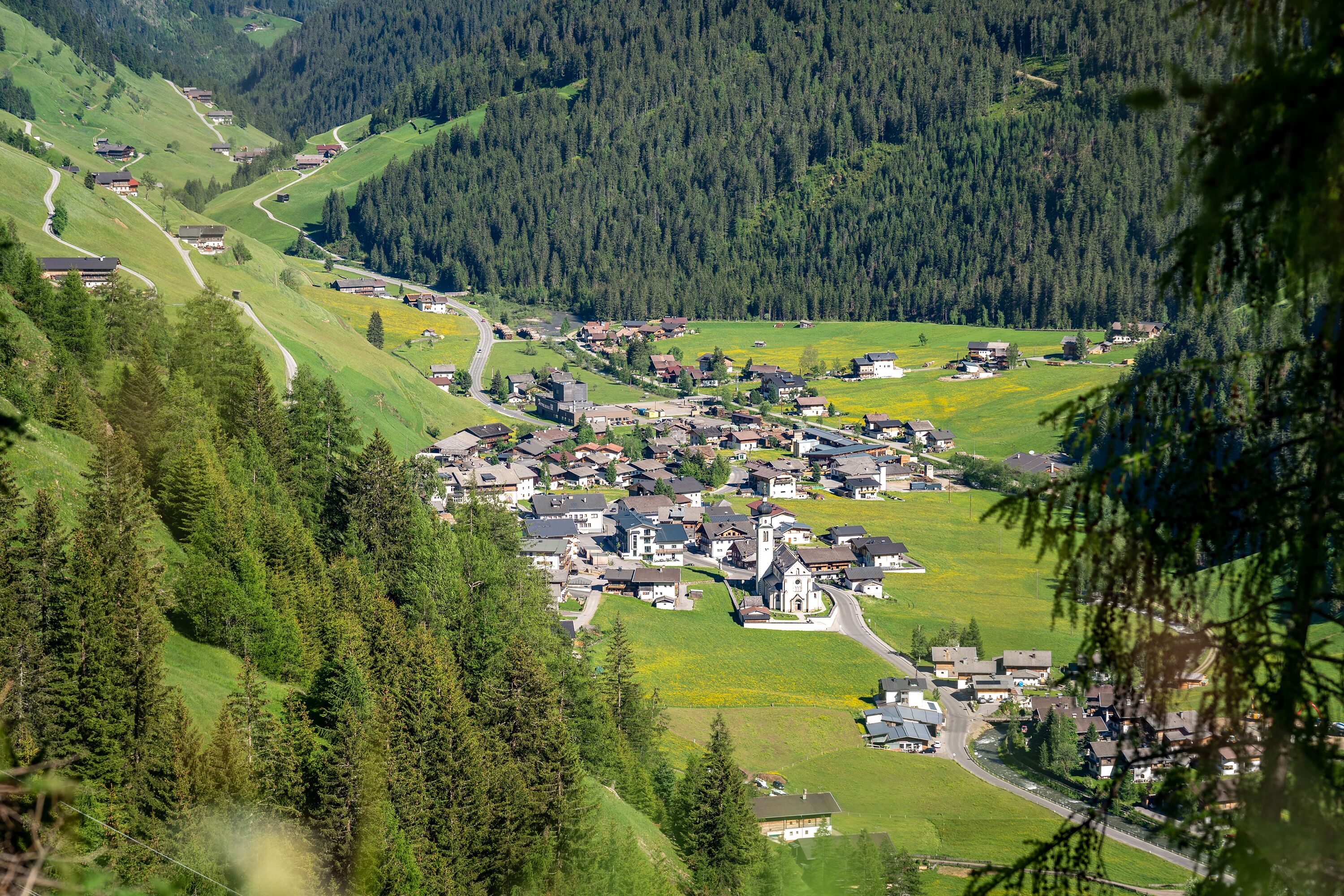 A mountainous village with houses and a church, surrounded by forest and fields.