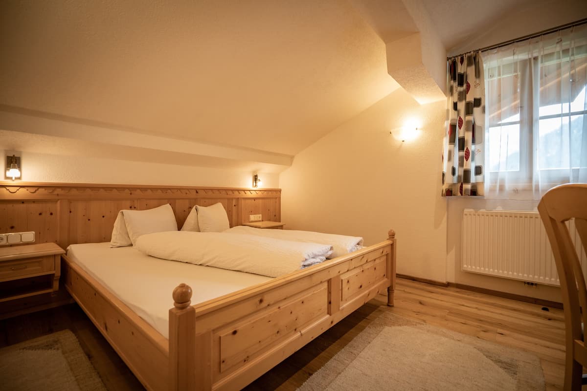 A bedroom with a wooden bed, bedside tables, a window with curtains, and a radiator.