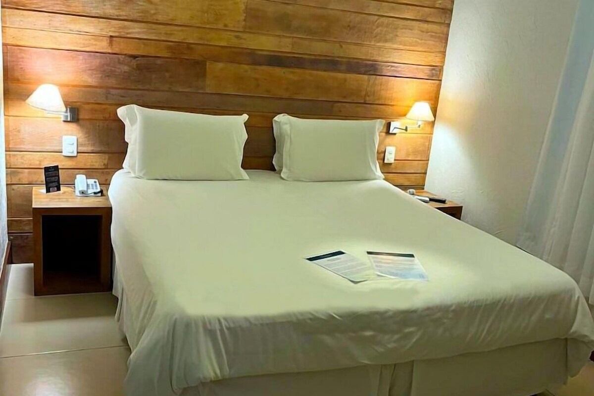 A neatly made bed with a wooden headboard, two bedside lamps, and a nightstand with a phone and a small table.