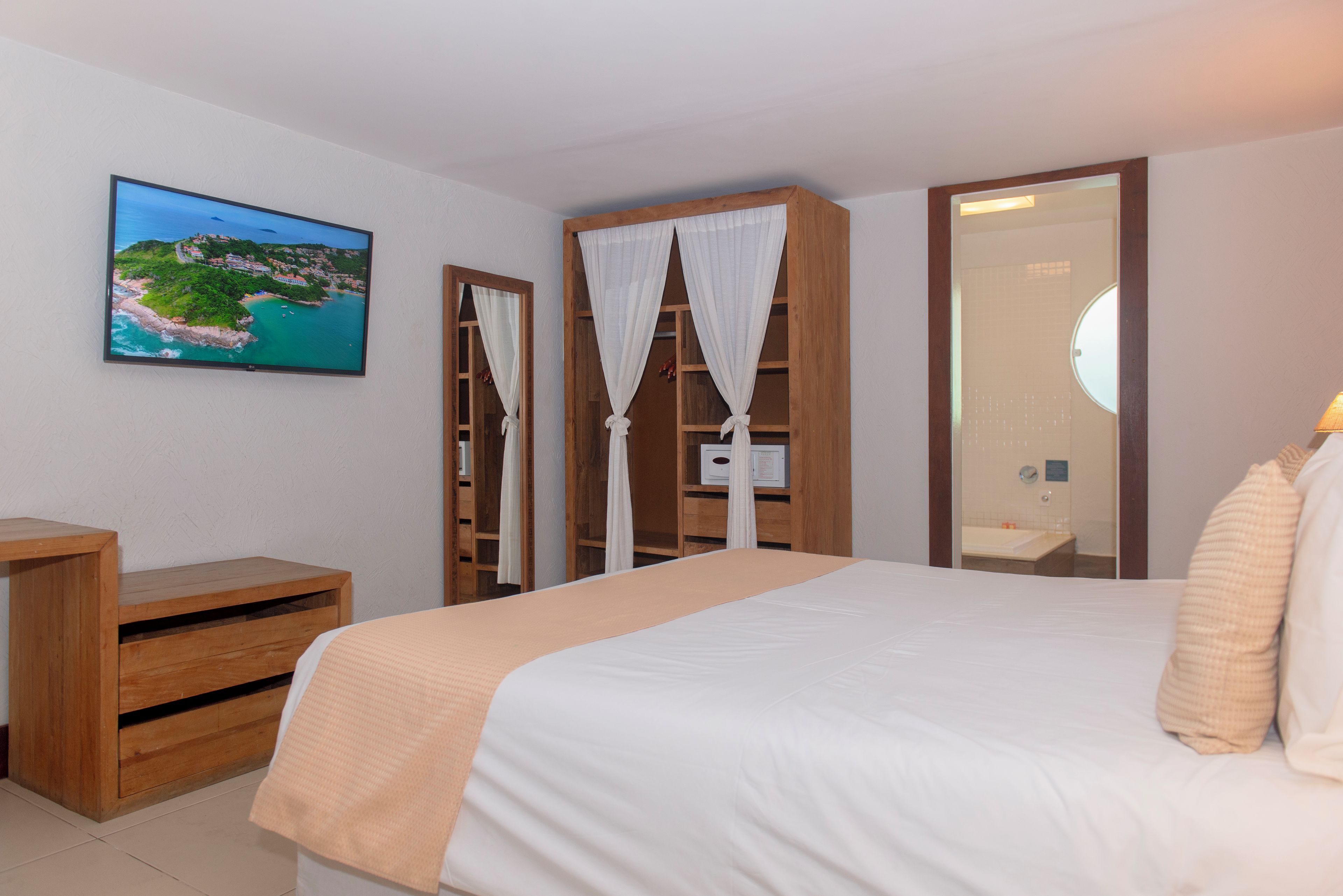 A bedroom with a bed, a wooden nightstand, a TV on the wall, and a bathroom visible through an open door.