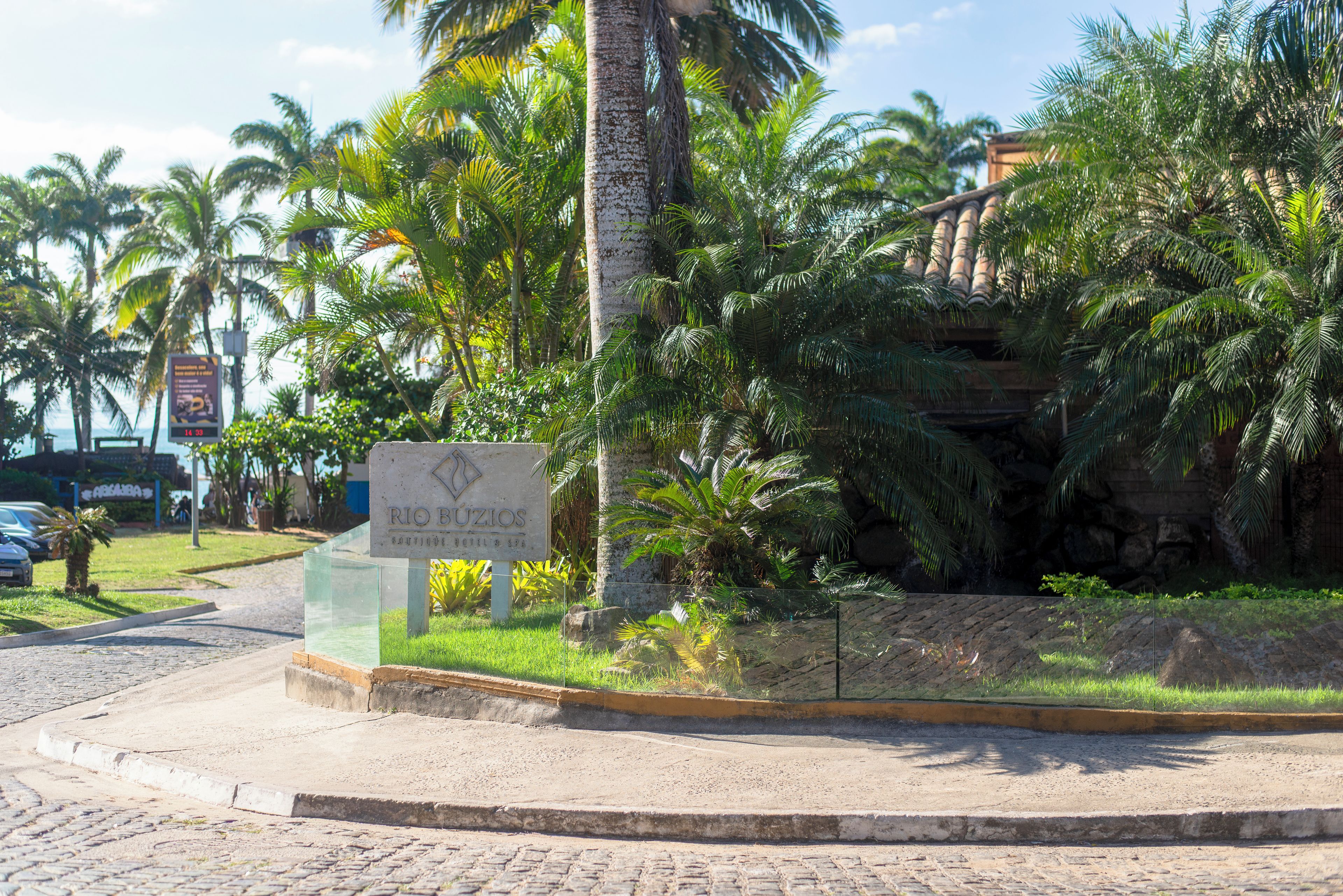 Een bordje voor Rio Buzios Boutique Hotel & Spa, omgeven door weelderige begroeiing en palmbomen.