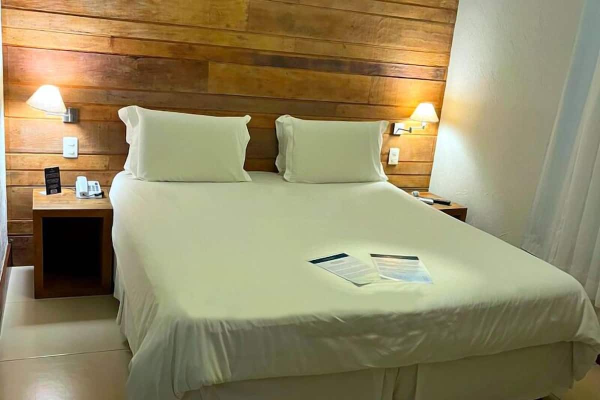 A neatly made bed with white linens, two bedside lamps, and a wooden headboard.