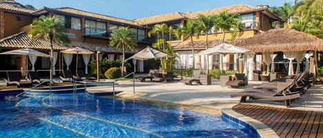 A resort with a swimming pool, lounge chairs, and palm trees.