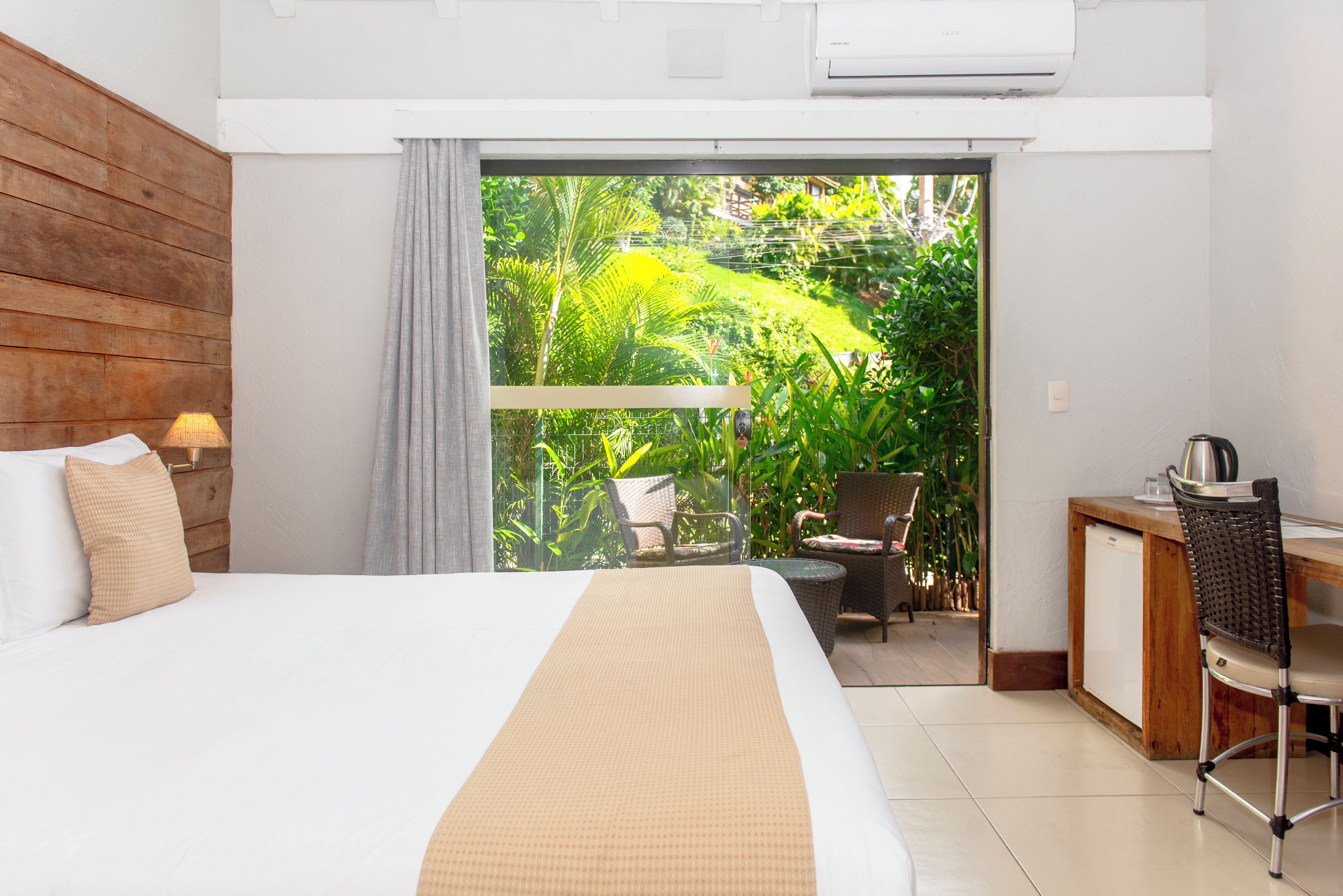 A hotel room with a bed, a desk, a chair, and a view of a garden through a sliding door.