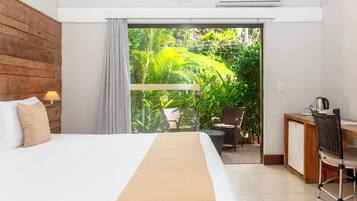 A hotel room with a bed, a desk, a chair, and a view of a garden through a sliding door.