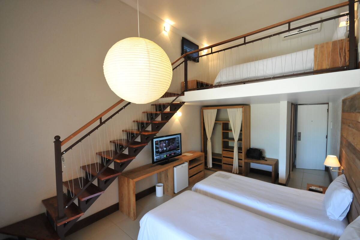 A bedroom with a bunk bed, a desk with a computer, a staircase, and a hanging light fixture.