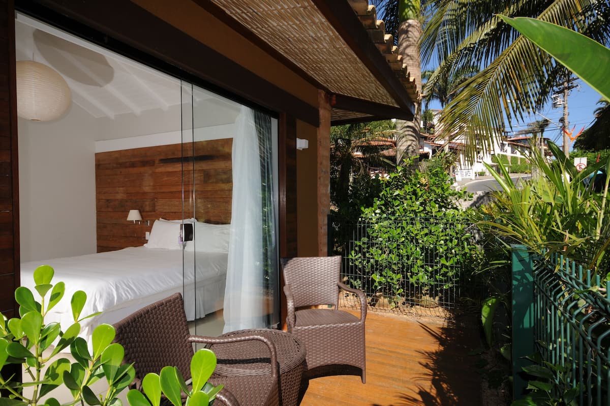 A bedroom with a large bed, a chair, and a view of a tropical garden.