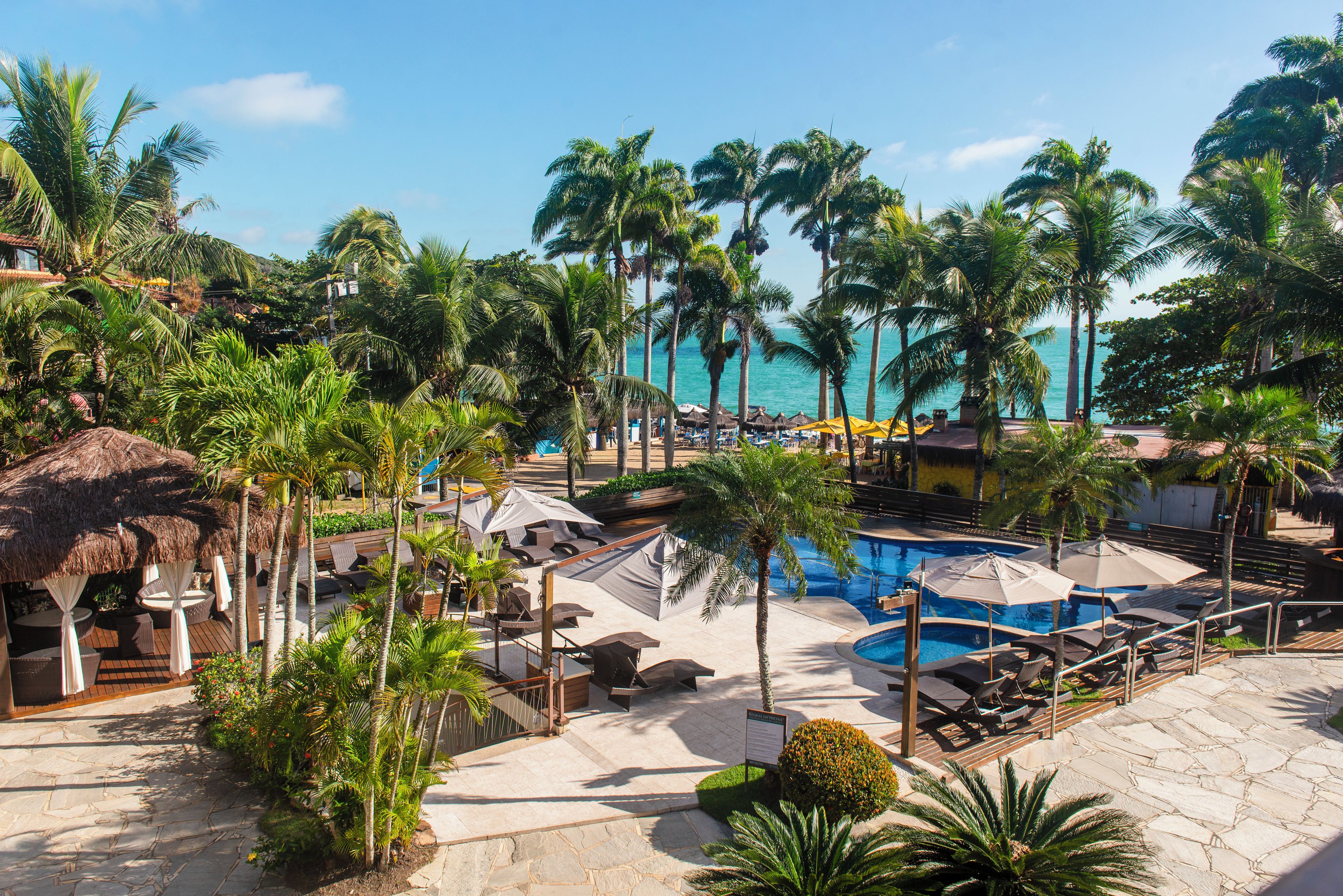 A resort pool area with lounge chairs, umbrellas, and palm trees.