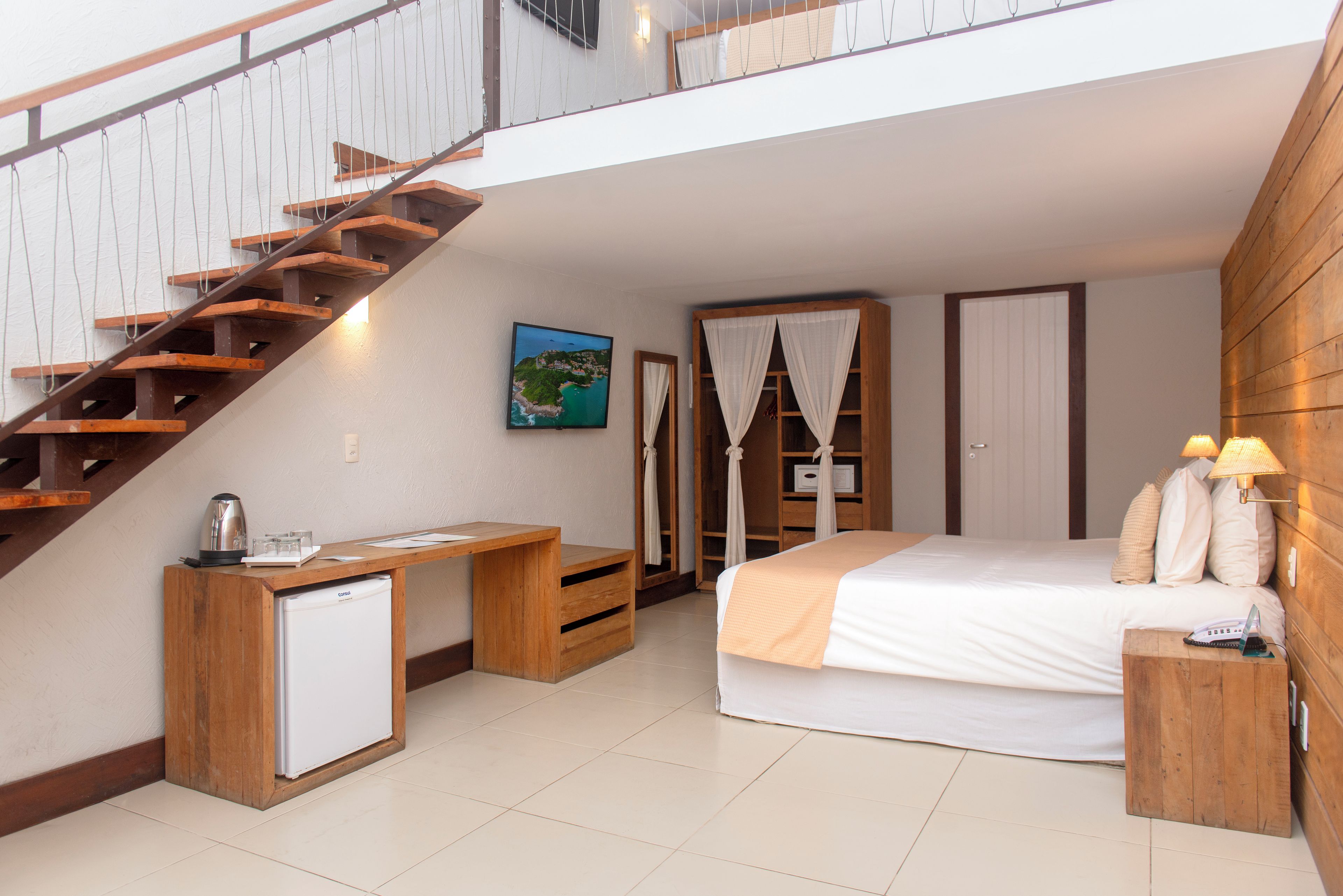 Une chambre à coucher comprenant un lit, un bureau, un petit réfrigérateur, une armoire et un escalier.