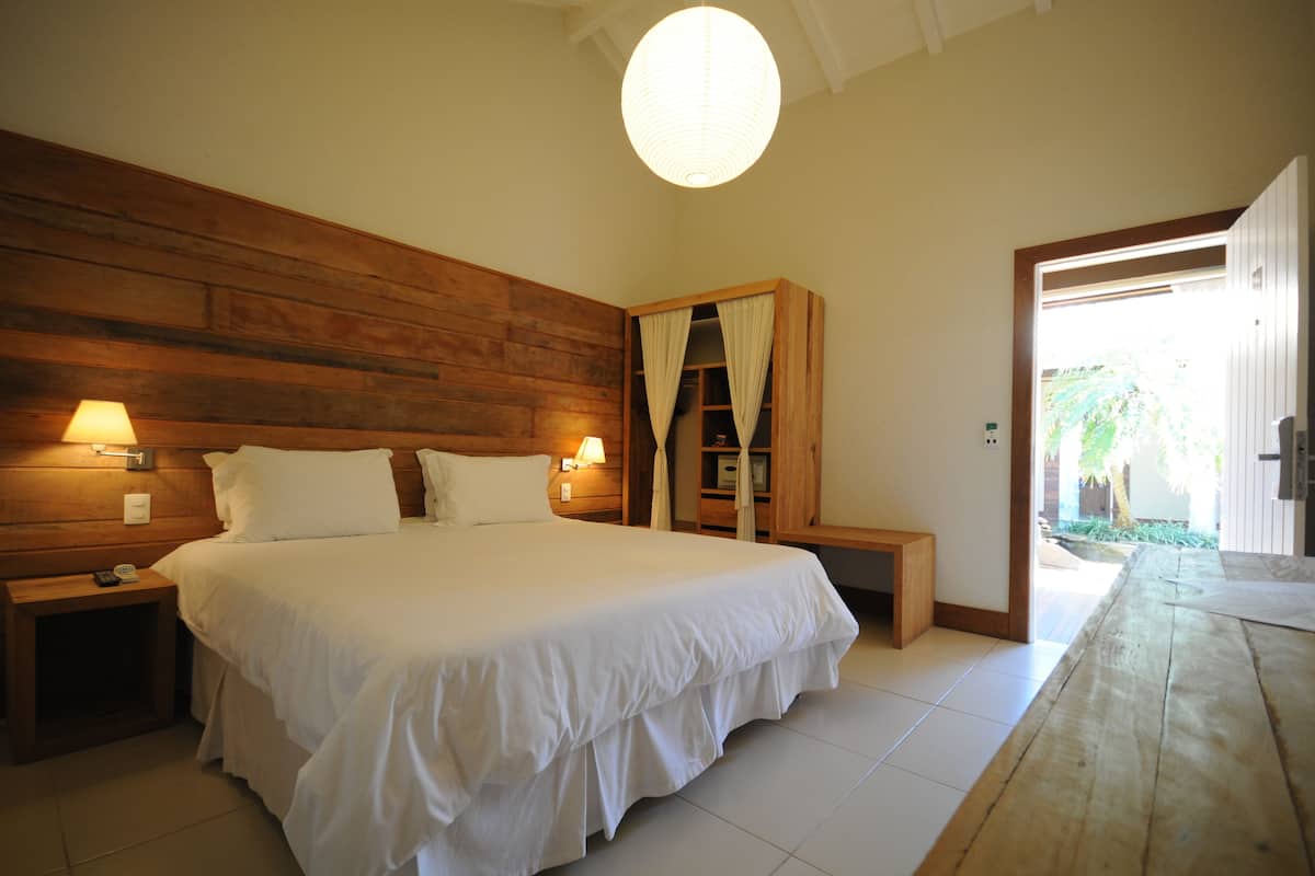 A bedroom with a large bed, wooden headboard, bedside lamps, a wooden nightstand, and a wooden bench.