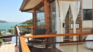 A balcony with wicker furniture, a glass door with curtains, and a view of the sea.
