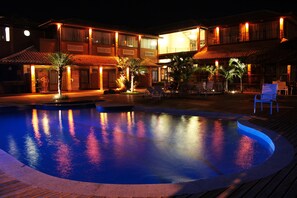 Un hotel con piscina, mobiliario exterior y fachada iluminada.