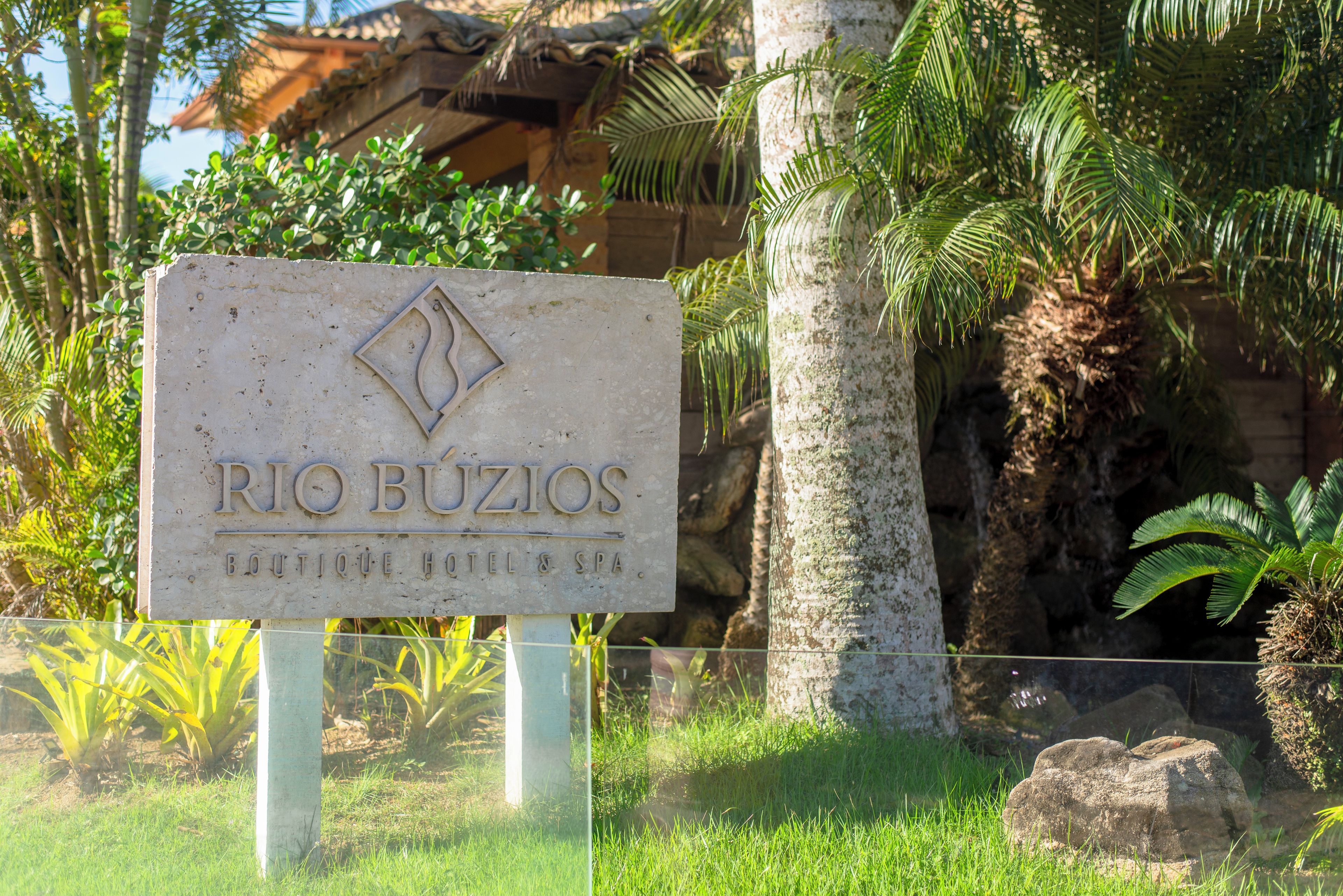 A sign for 'RIO BUZIOS BOUTIQUE HOTEL & SPA' with a tropical backdrop.