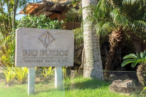 Letrero que indica 'RIO BUZIOS BOUTIQUE HOTEL & SPA' con un fondo tropical.