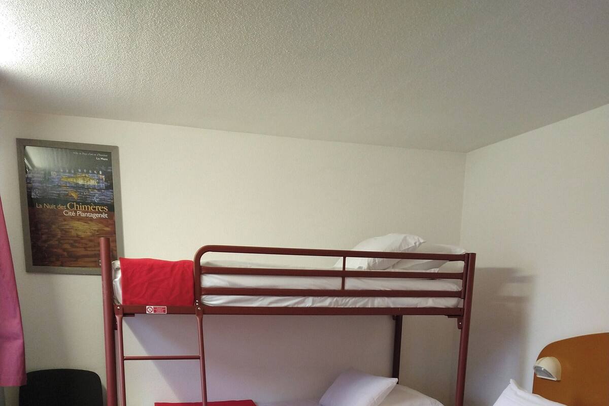 Une chambre avec un lit superposé, un bureau et une chaise, une affiche accrochée au mur et une tête de lit en bois.