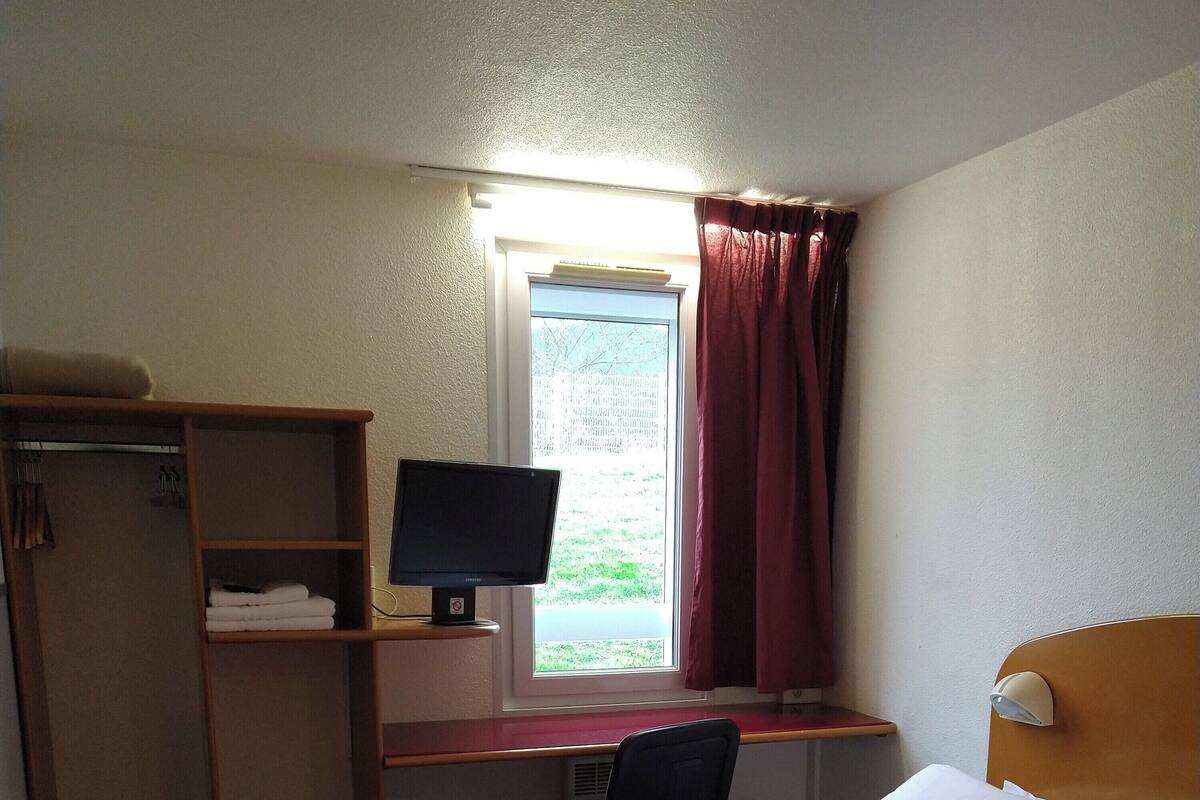 Une chambre d’hôtel avec deux lits, un bureau avec un ordinateur, une armoire et une fenêtre avec des rideaux.