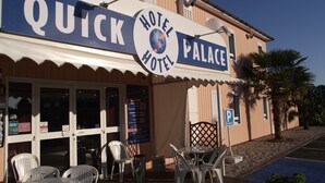 The exterior of a hotel named "Quick Hotel Palace" with a signboard, outdoor seating area, and a parking sign. - Quick Palace Le Mans Nord St Saturnin (Saint-Saturnin)