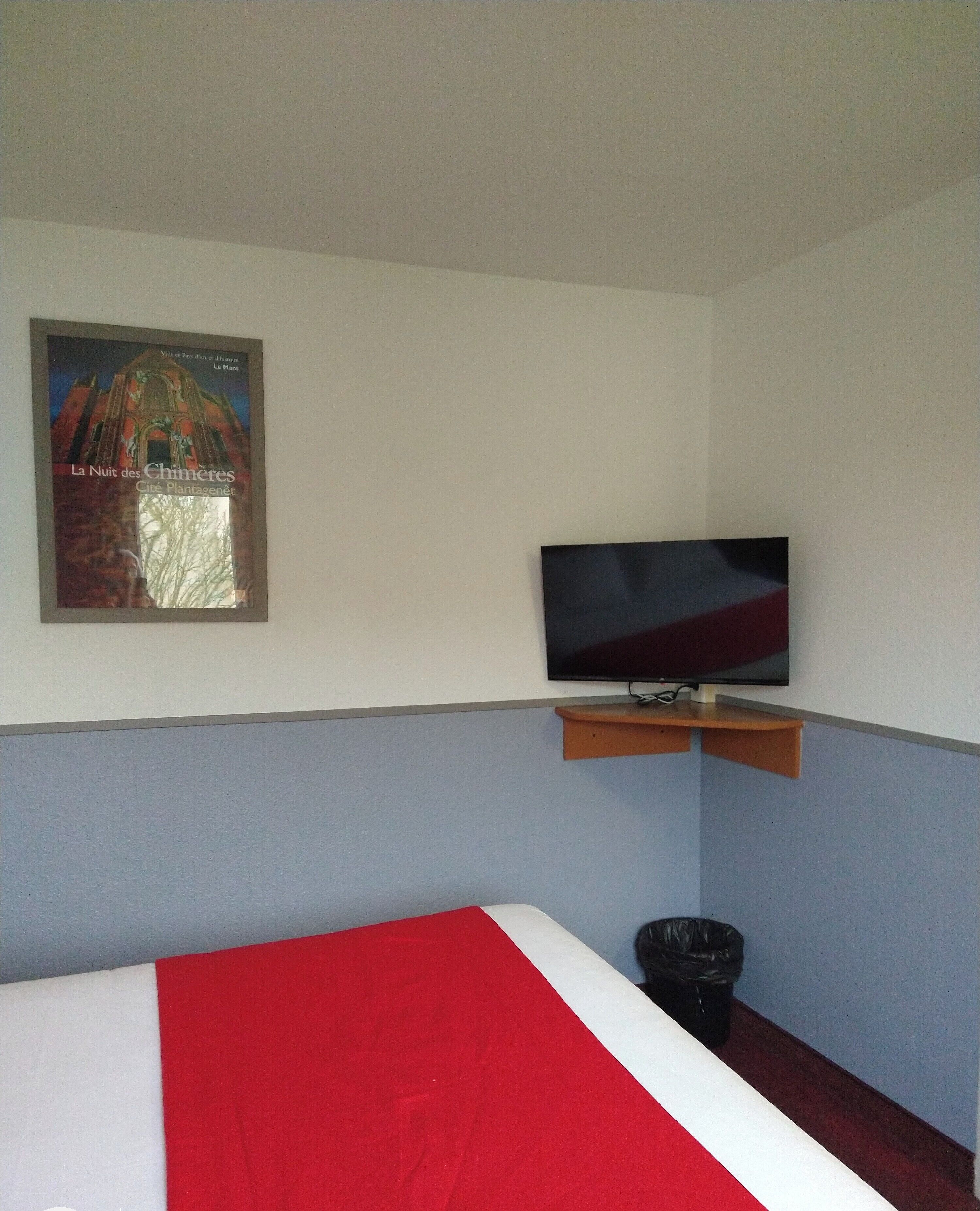 Habitación de hotel con cama, televisor montado en un estante de madera y un cartel en la pared.