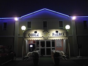 Un hôtel appelé « Quick Palace », doté d’une enseigne lumineuse, d’un parking et d’une terrasse.