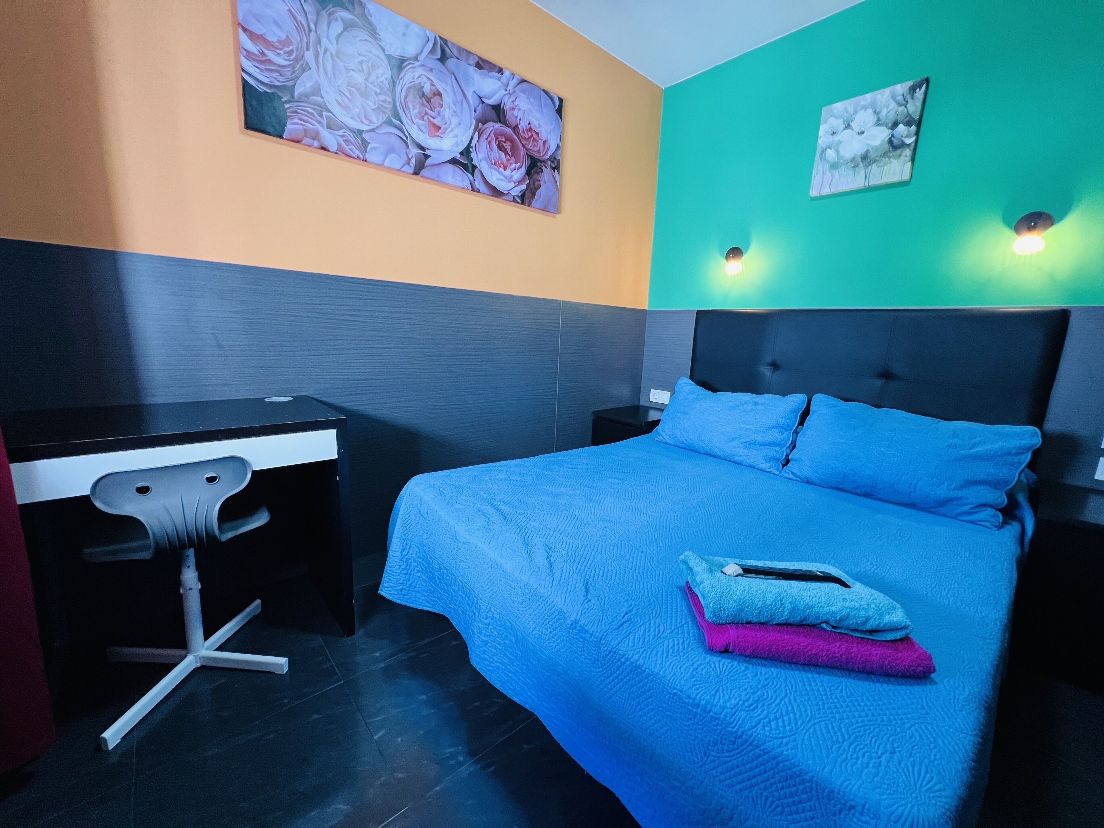 A modern bedroom with a large bed, a desk, and two wall-mounted lights.