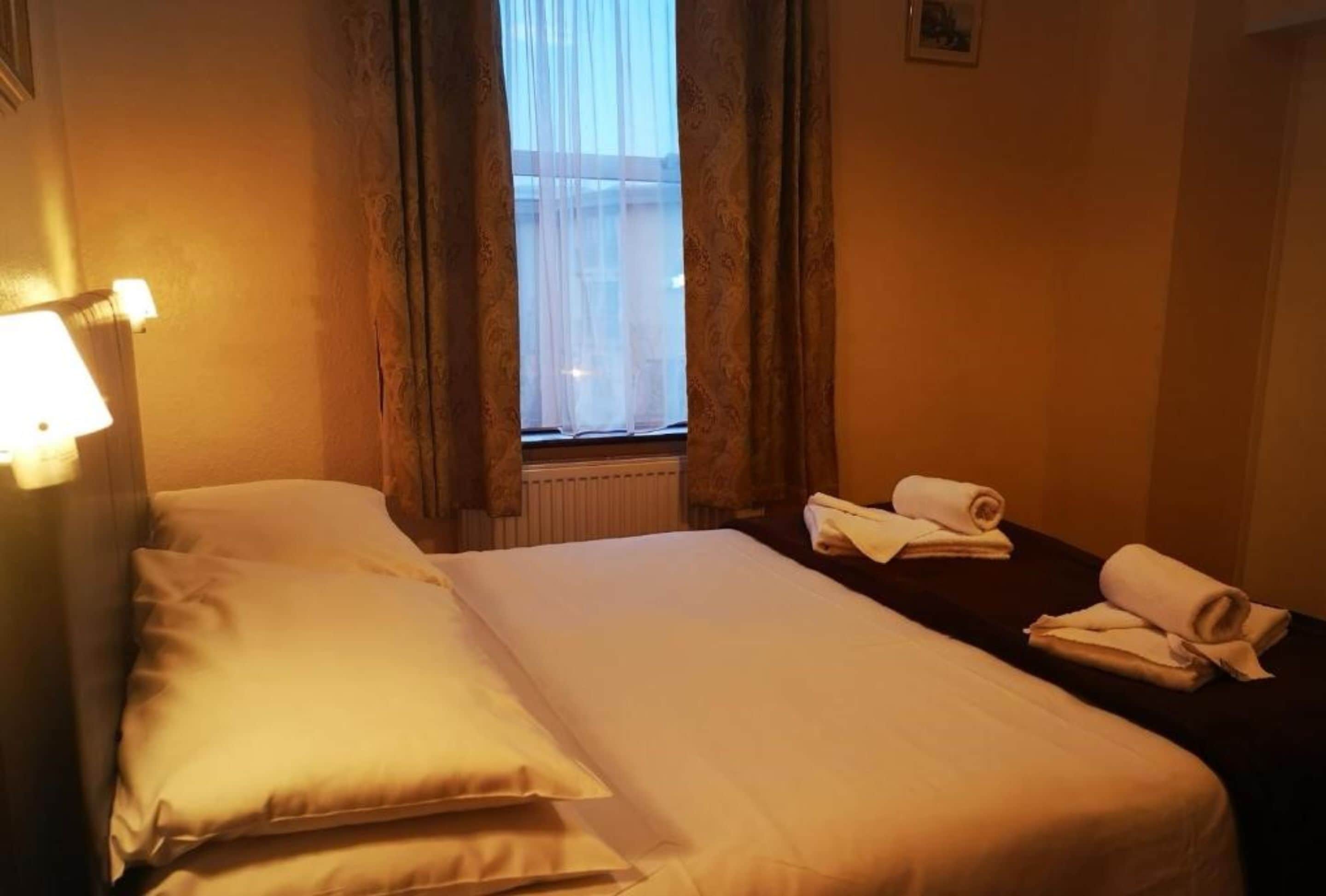 Ein Hotelzimmer mit Bett, Nachttisch und einem mit Vorhängen versehenen Fenster.