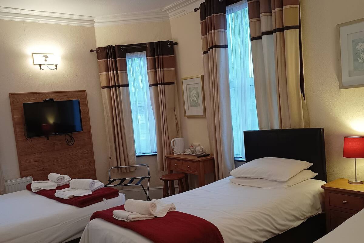 A hotel room with two beds, a TV, a desk, a chair, and a window with curtains.